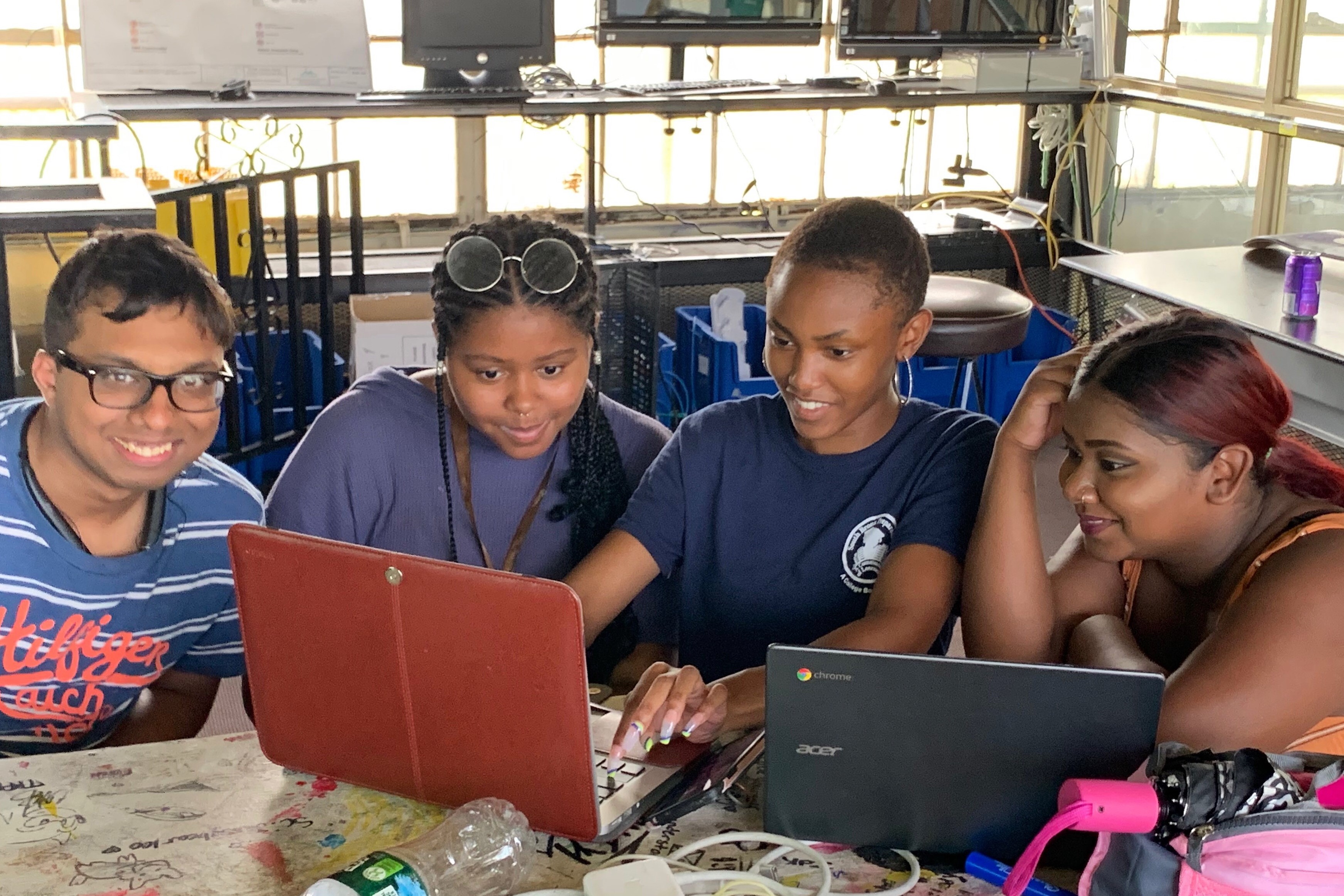 4 teenagers looking at a computer and smiling